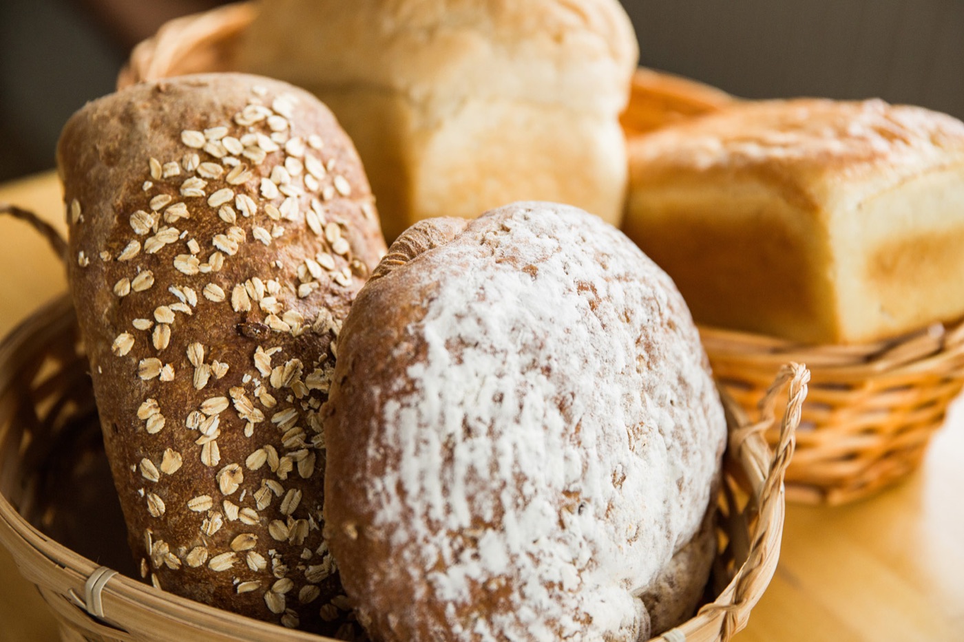 A basket of fresh-baked loaves, including oat-topped and flour-dusted breads