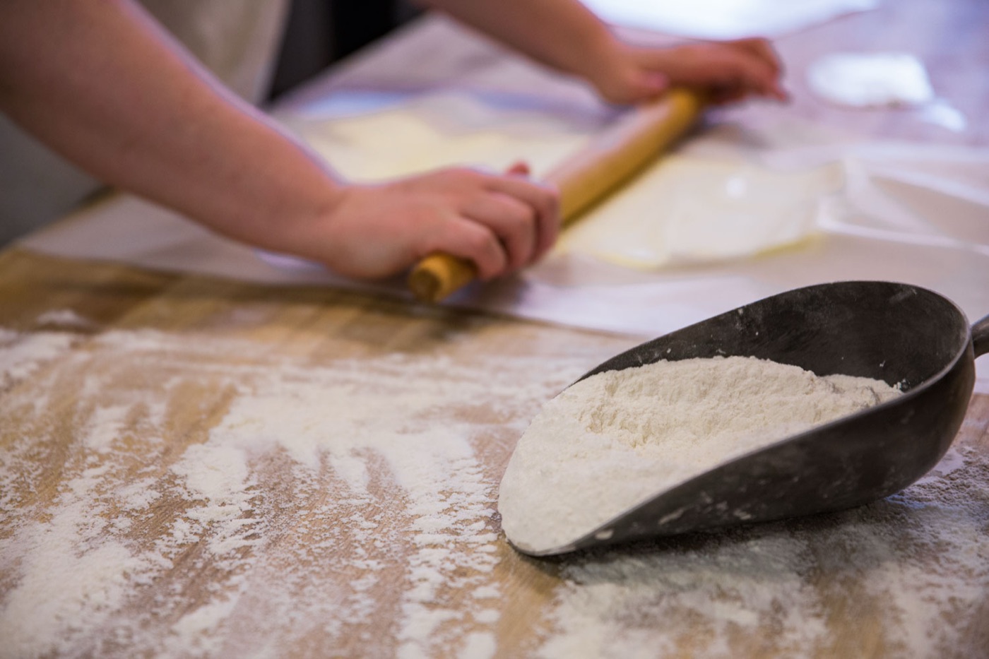 A baker rolling dough beside a scoop of flour